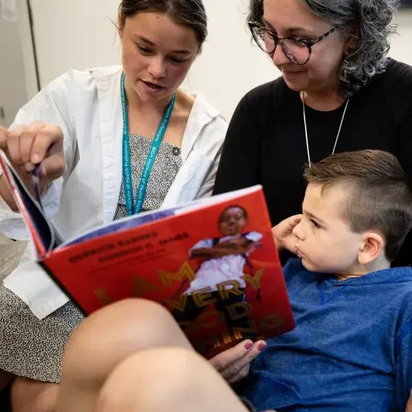A doctor, young child, and a woman all looking at a book