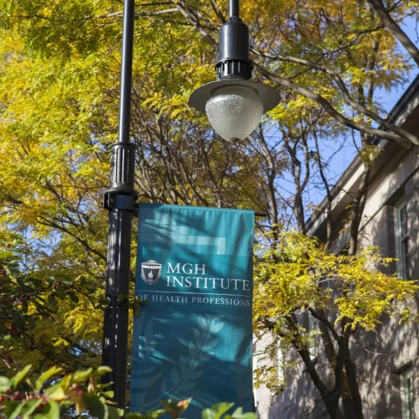 Lamp post with University logo flag in front of tree foliage in the sunlight
