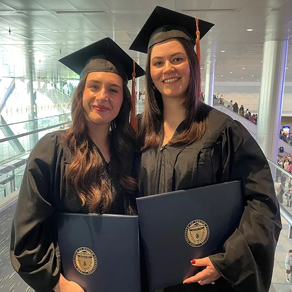 Two women wearing graduation gowns and caps while holding diplomas