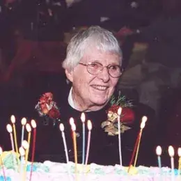 photo taken at a party - marjorie smiles over a cake with lots of candles and wears a corsage of roses