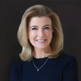 woman with blond hair styled in a wave back from her head wearing a navy top and silver necklace