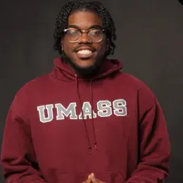 Ronald Dessources has glasses and black braids. He is wearing a red UMASS sweatshirt.