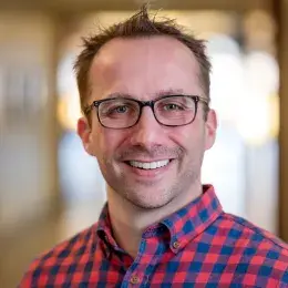 Christopher Joyce has short hair, is wearing glasses, and a red and blue checkered shirt