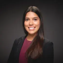 Daniela Diaz Caro has long, straight brown hair. She is wearing a black blazer and a burgundy top.