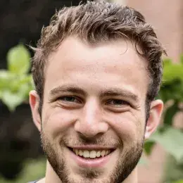 Man with short brown hair wearing a purple shirt smiling and looking at camera