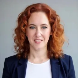 Headshot of Woman with wavy red hair wearing a white shirt and a blue jacket