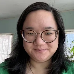 Headshot of woman with long black hair wearing glasses and a green shirt