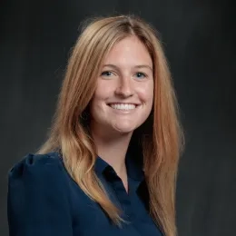 Woman with long blonde hair wearing a blue collared shirt in front of a black background