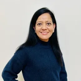 Headshot of woman with long black hair wearing a blue long sleeve shirt against a white background