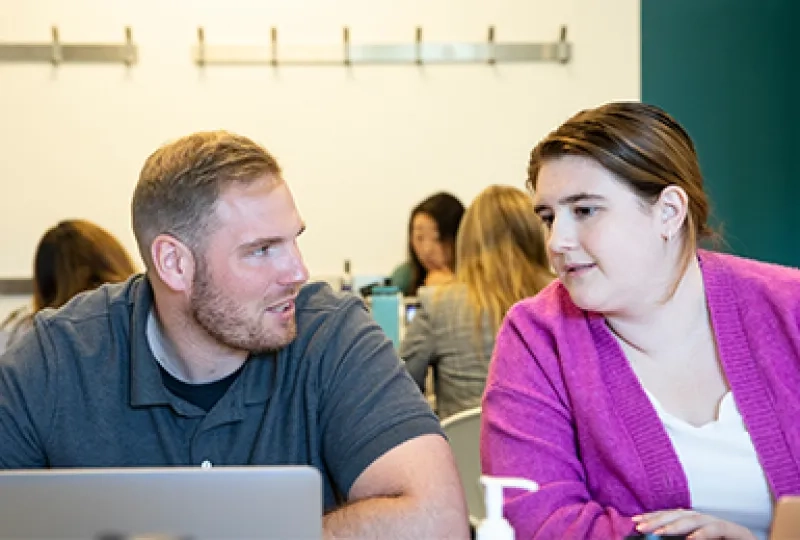 a woman leans over to look at a laptop while a man talks to her