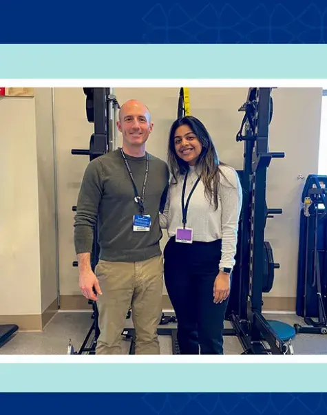 two people pose together in front of a room of exercise equipment