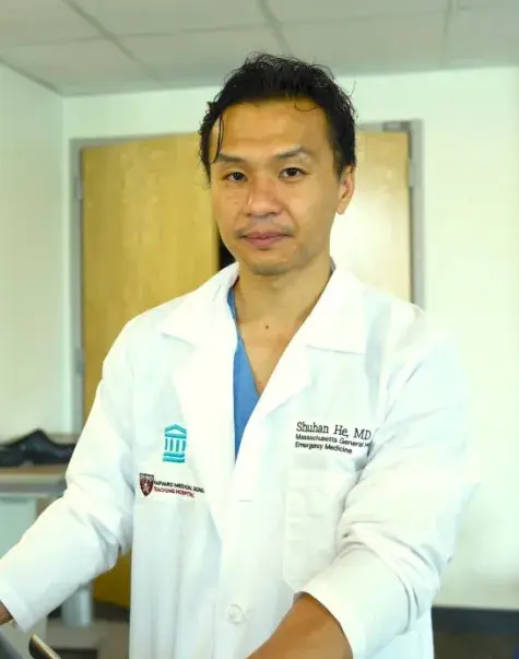 Doctor in lab coat looking into camera; coat has name and hosital affiliation 