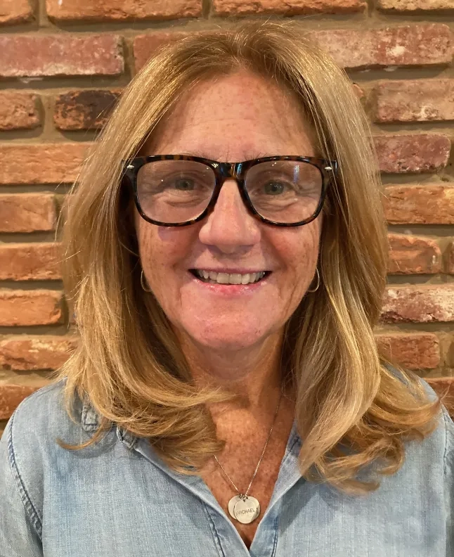 ann wears glasses and is in front of a brick wall