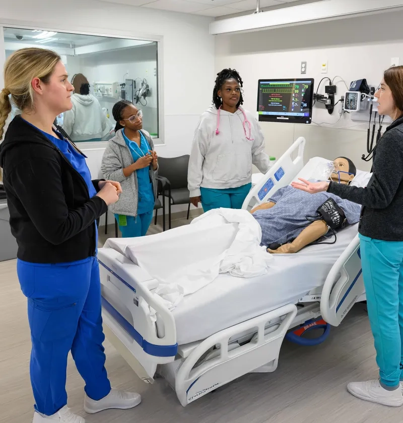 nursing students stand around a manikin in a hospital bed