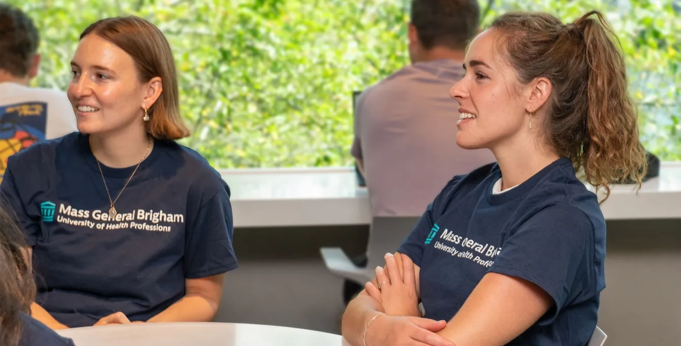 two women with Mass General Brigham University tshirts sit at a table